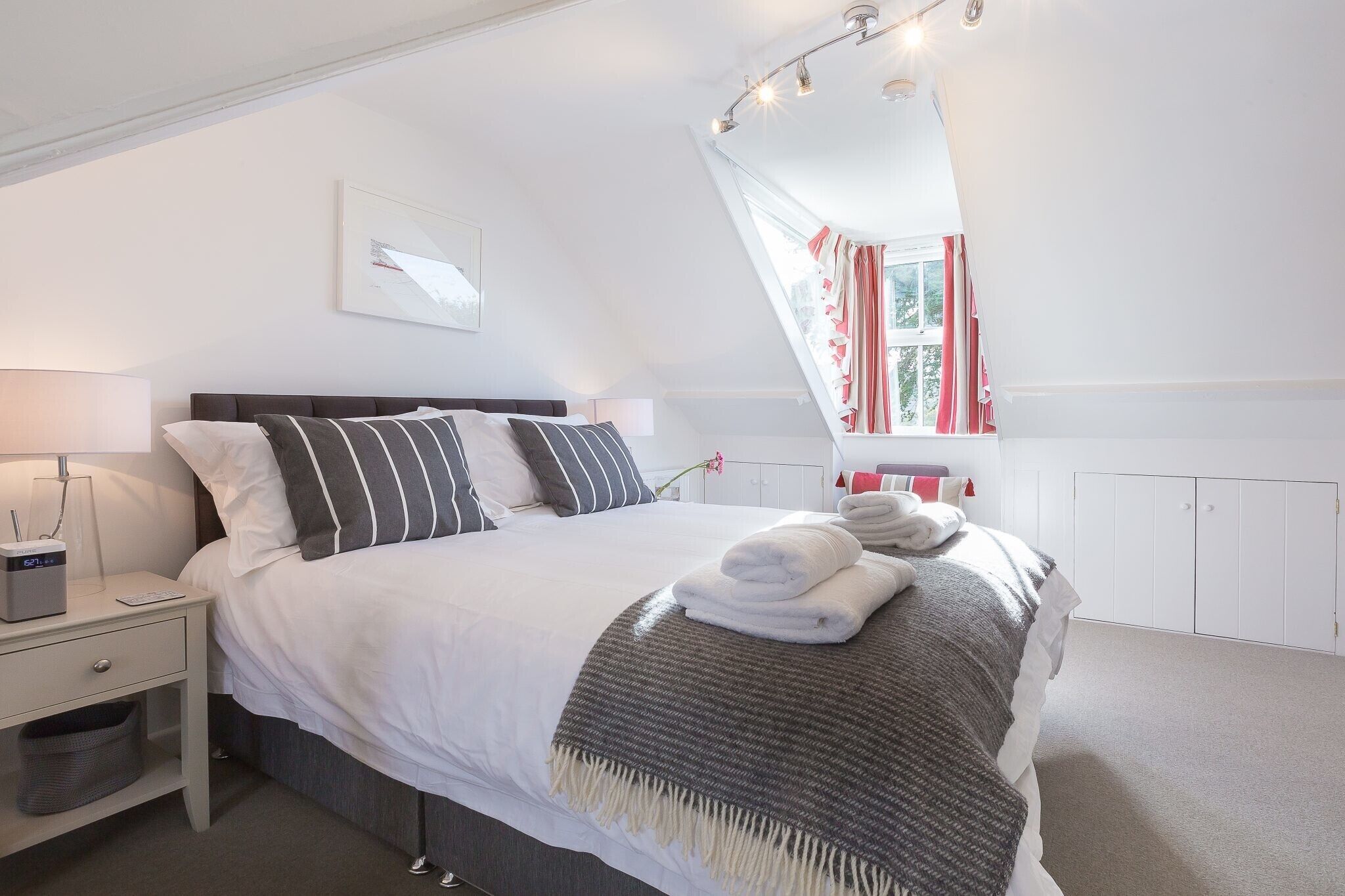 A neatly made bed with white and striped pillows, a grey throw blanket, and folded towels.