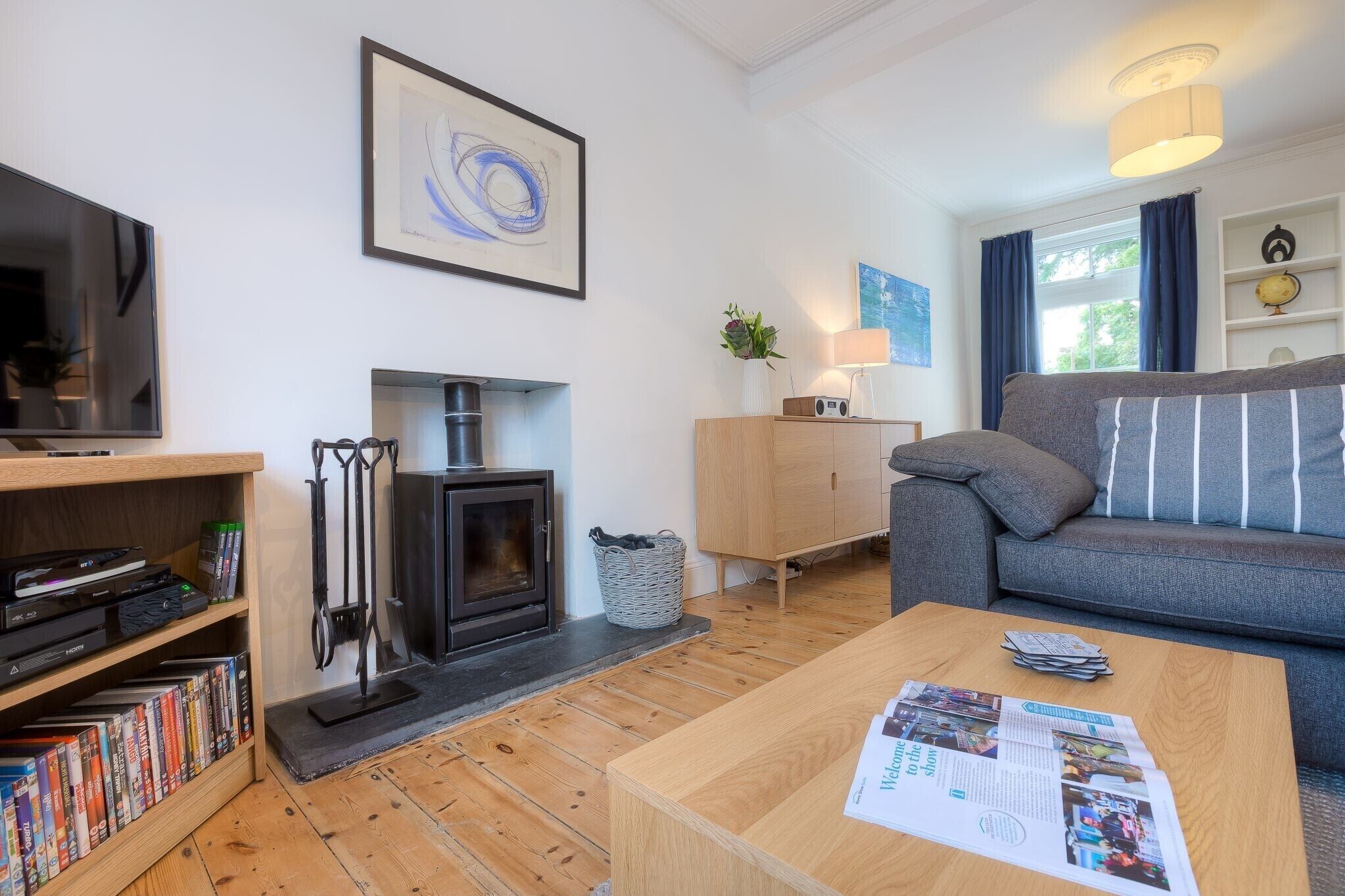 A modern living room with a fireplace, a sofa, a coffee table with magazines, and a TV on a stand.