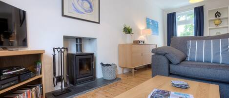 A modern living room with a fireplace, a sofa, a coffee table with magazines, and a TV on a stand.