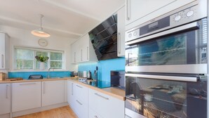 A modern kitchen with white cabinets, a blue backsplash, and stainless steel appliances. - Sea Dream (St Ives)