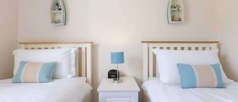 Une chambre avec deux lits jumeaux, une table de chevet avec une lampe et des étagères décoratives fixées aux murs.