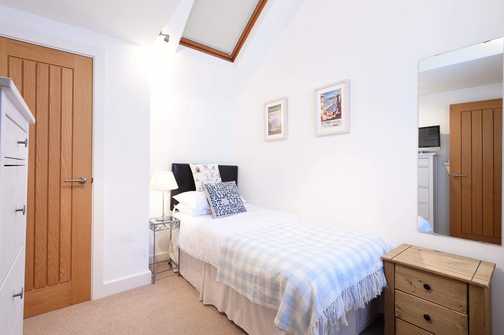 A bedroom with a bed, bedside table, lamp, and a mirror.