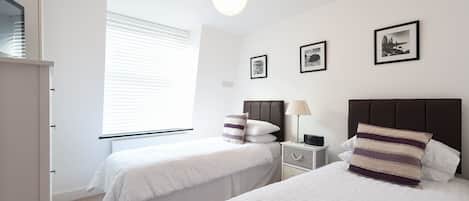 Ein Schlafzimmer mit zwei Betten, einem Nachttisch, einer Lampe und gerahmten Bildern an der Wand.