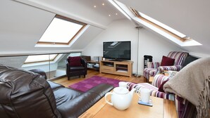 A modern loft bedroom with skylights, a large TV, a sofa, and a coffee table.