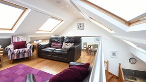 A high-ceilinged living room with a skylight, a black leather sofa, a striped armchair, and a purple rug.