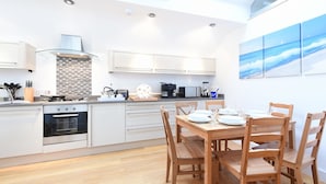A modern kitchen with white cabinets, a wooden dining table, and a view of the sea through a skylight.