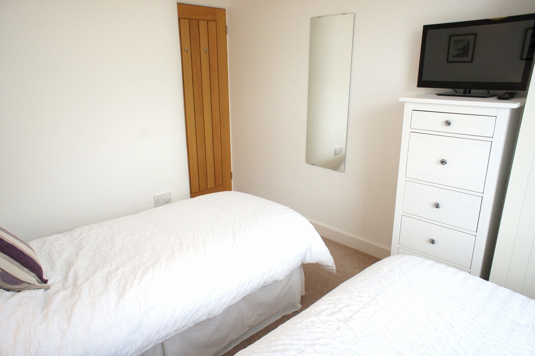 A bedroom with two beds, a wooden wardrobe, a dresser with drawers, and a television on top.