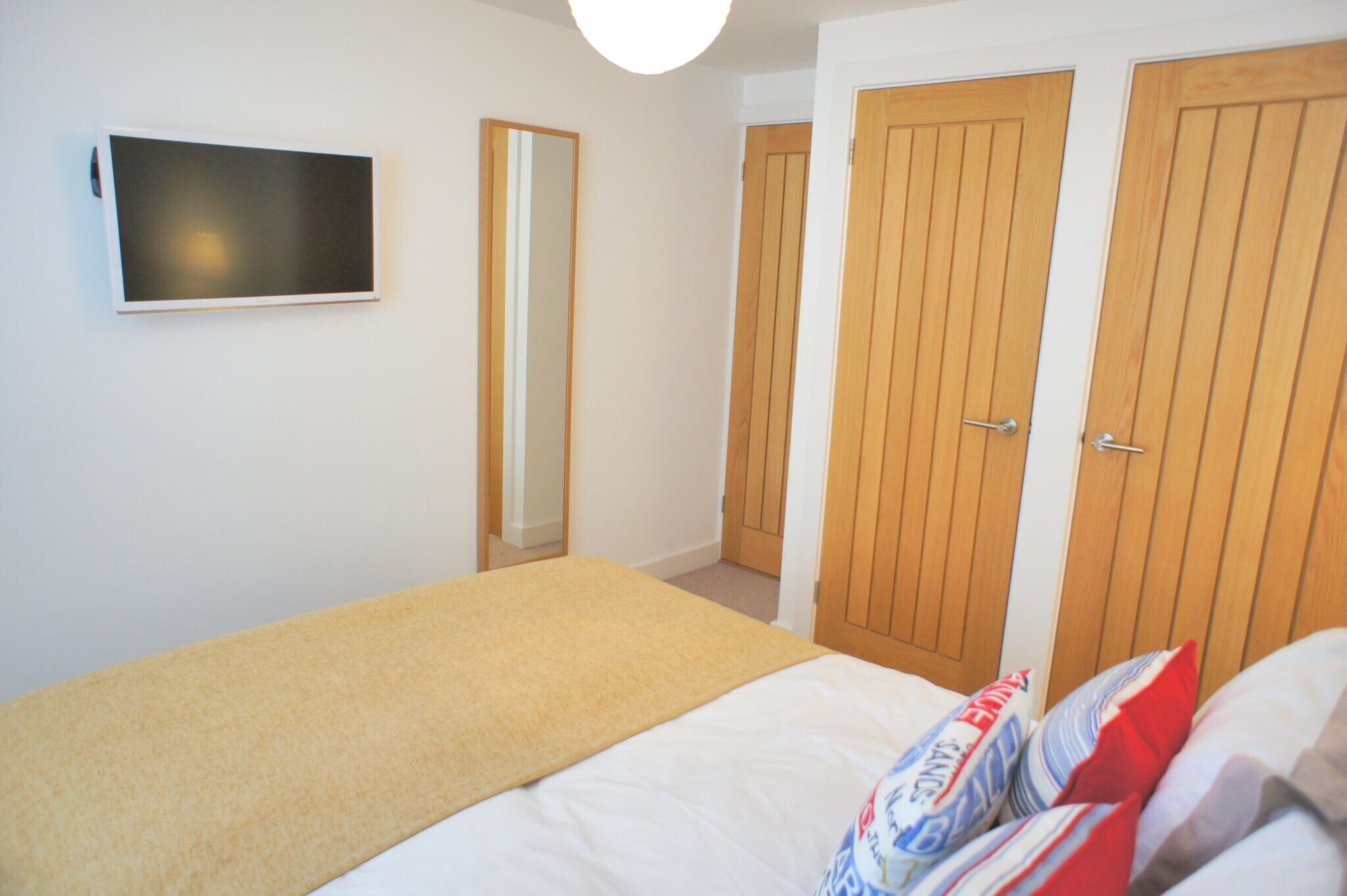 Een slaapkamer met een bed, een aan de muur bevestigde televisie en houten deuren.