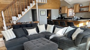 A modern living room with a sectional sofa, ottoman, and a staircase leading to another level.
