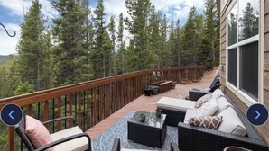 A deck with outdoor furniture, a view of trees, and a house in the background.