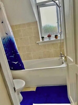 A bathroom with a bathtub, a toilet, and a window with a view of greenery.