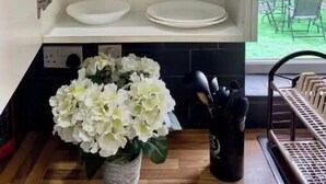 An open kitchen cabinet with white shelves, a vase of white flowers, and a utensil holder. - Modern, spacious and comfortable 3 bedroom home. (Manchester)