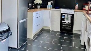 A modern kitchen with white cabinets, a stainless steel refrigerator, a black range hood, and a black tiled floor. - Modern, spacious and comfortable 3 bedroom home. (Manchester)