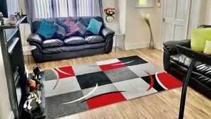 A living room with a black leather sofa, a patterned rug, and a white door. - Modern, spacious and comfortable 3 bedroom home. (Manchester)