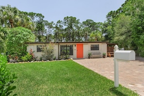 A single-story building with a red door, surrounded by a well-maintained lawn and various plants.