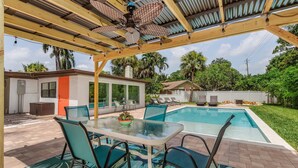 An outdoor patio with a glass table and chairs, a ceiling fan, and a swimming pool. - "Flamingo Feliz" Heated Pool! Close to Beach and 5th Ave. (Naples)