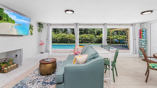A spacious living area with a large TV, a fireplace, a pool view, and a dining area with outdoor seating. - "Flamingo Feliz" Heated Pool! Close to Beach and 5th Ave. (Naples)