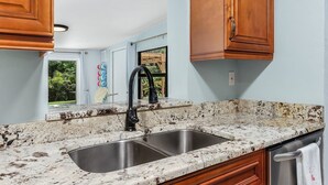A kitchen with granite countertops, a stainless steel sink, wooden cabinets, and a window with a view of greenery. - "Flamingo Feliz" Heated Pool! Close to Beach and 5th Ave. (Naples)