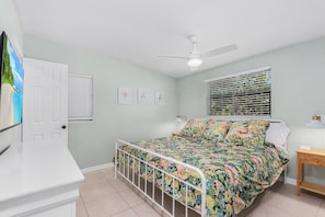 A bedroom with a bed, a ceiling fan, a window with blinds, and a door.