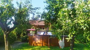 Un área de estar al aire libre con madera, una sombrilla roja, una parrilla de barbacoa y una silla blanca.