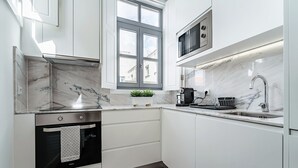 Una cuina moderna amb armaris blancs, forn integrat, microones i finestra amb vista a edificis.