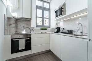 A modern kitchen with white cabinets, a built-in oven, a microwave, and a window with a view of buildings. - Nomad's Formosa Harmony - 1BED Porto (Porto)