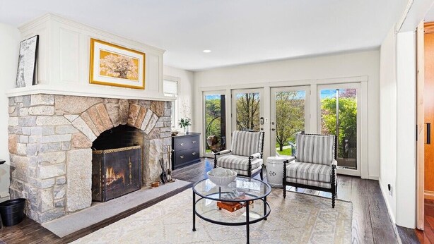 A living room with a stone fireplace, two armchairs, a coffee table, and large windows.