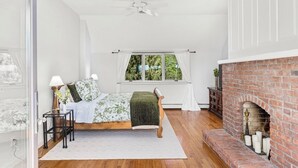 A bedroom with a bed, a window with curtains, a fireplace, and a ceiling fan.