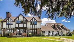 A traditional Tudor-style house with a symmetrical facade, multiple chimneys, and a well-maintained lawn.
