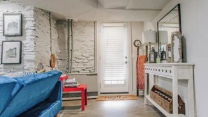 A living room with a stone wall, a blue sofa, a red table, and a white console table with a mirror. - Stunning Ground Floor Apartment in Green Ridge. (Scranton)