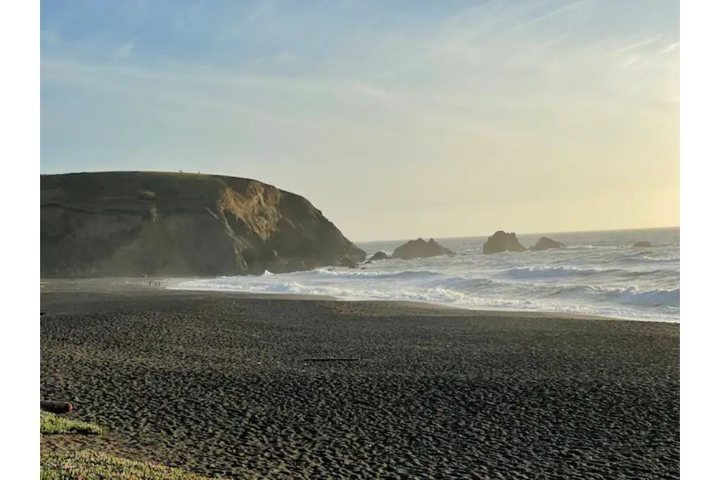 A beach with a rocky cliff and waves crashing onto the shore.