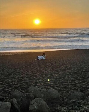 Un coucher de soleil sur une plage, avec des rochers au premier plan.