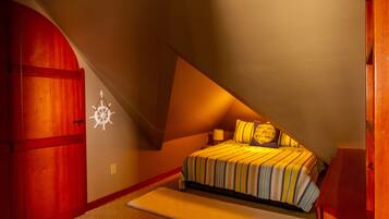 A bedroom with a sloped ceiling, a bed with striped bedding, a wooden wardrobe, and a wall decoration.