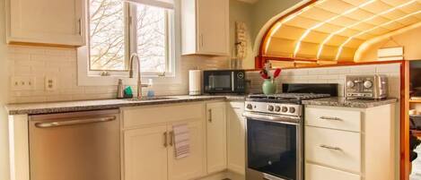 A kitchen with white cabinets, a dishwasher, a stove, a microwave, and a toaster.