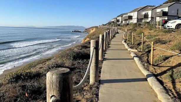 Un paseo marítimo con sendero de concreto, postes de madera y una hilera de casas.
