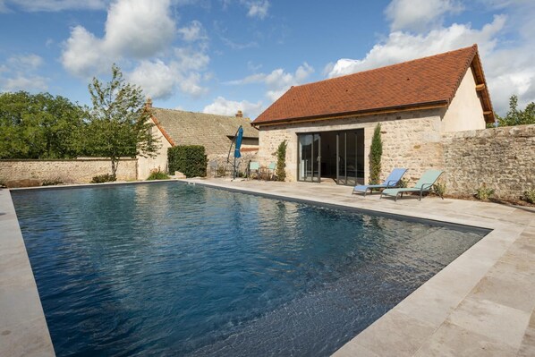 A swimming pool with a stone wall, a building with a tiled roof, and a clear sky.