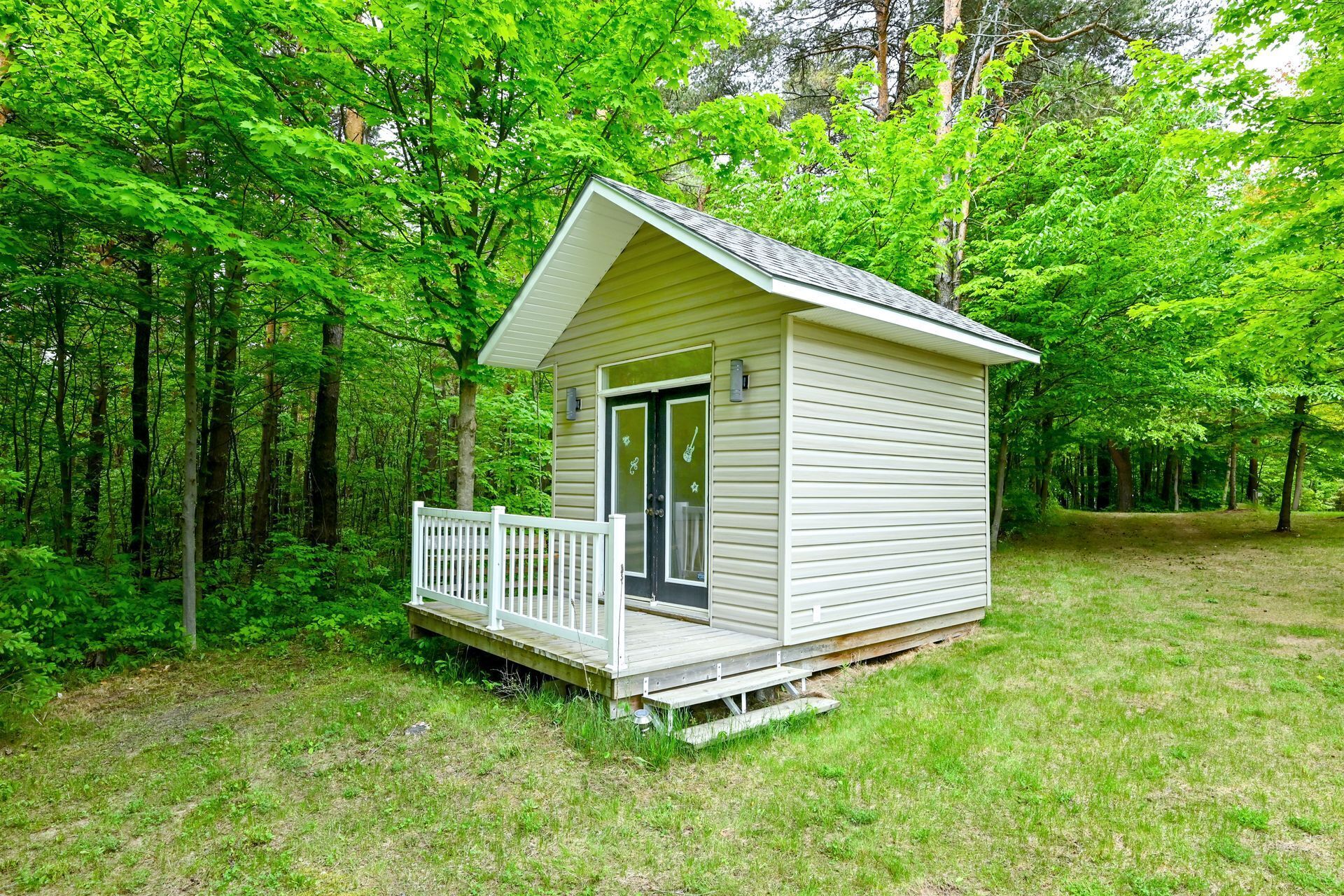 A small, single-story cabin with a porch, surrounded by dense green trees.