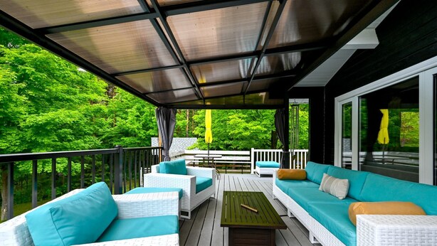 A covered outdoor seating area with white wicker furniture and teal cushions, surrounded by a wooden deck and glass railings.