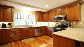 Una cocina con armarios de madera, lavavajillas de acero inoxidable, microondas y estufa.