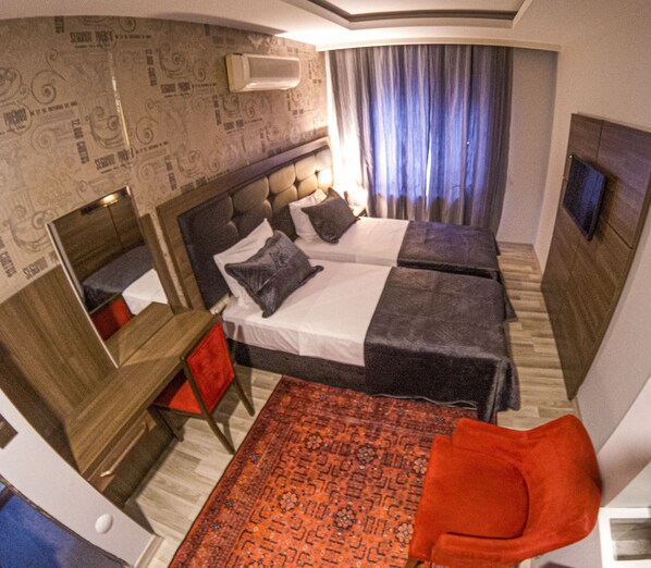 A hotel room with two beds, a desk, a chair, a TV, and a patterned rug. - NEW AKÇAABAT HOTEL (Akçaabat)