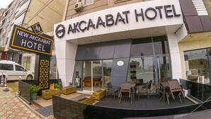 L’extérieur de l’hôtel Akcaabat, avec son panneau indicateur, son espace extérieur aménagé avec des sièges et un fourgon blanc garé à proximité.
