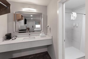 A modern bathroom with a large mirror, two sinks, a shower, and a coffee machine.