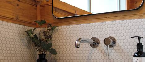 A bathroom with a white sink, a mirror above it, and a plant on the left.