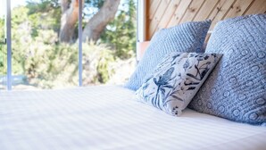 Een bed met gestreepte kussens en uitzicht op bomen door een raam.