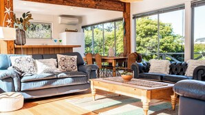 Een moderne woonkamer met houten vloer, een zwart lederen bank, een houten salontafel en een eettafel met stoelen.