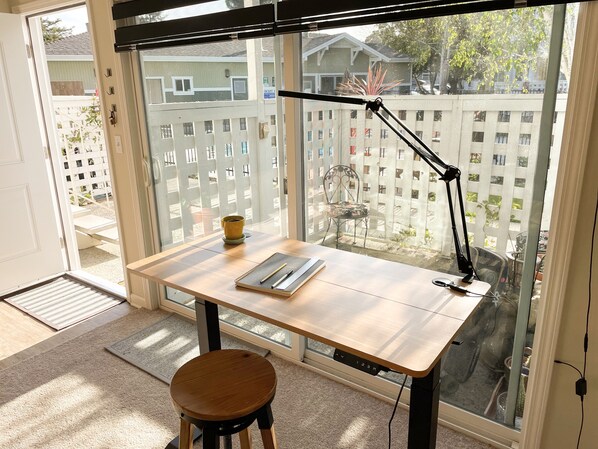 Une petite pièce bien éclairée, avec un bureau en bois, une chaise et une grande fenêtre.