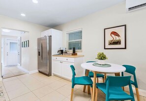 A modern kitchen with white cabinets, a stainless steel refrigerator, and a dining area with teal chairs and a white table.