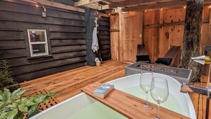 A cozy cabin interior with a wooden floor, a large bathtub, and a fireplace.