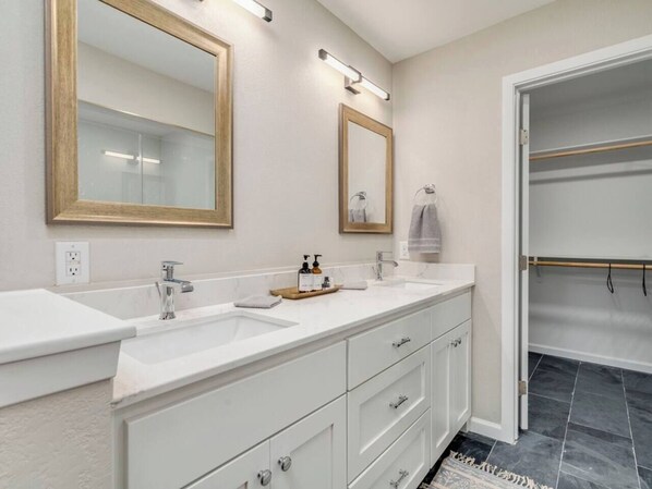 A modern bathroom with two sinks, a mirror, and a walk-in closet.