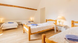 A room with three wooden beds, each with a bedside table and lamp, in a simple, clean design with wooden beams on the ceiling.